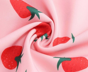 Close-up of pink fabric featuring red strawberry print with green leaves and soft texture