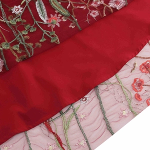 Detail of red mesh dress showing intricate floral embroidery with green leaves and red flowers