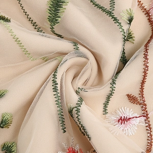 Detailed macro view of beige mesh fabric featuring delicate floral and vine embroidery
