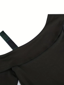 Detail of elegant black dress showing a dark green twill strap and folded neckline detail