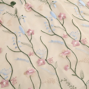 Macro shot of floral embroidery on fine beige mesh with pink and blue flowers