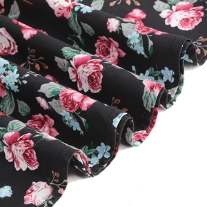 Detailed view of floral print fabric with pink roses and green leaves on black background