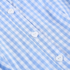 Détails des boutons blancs en forme de cœur sur le tissu vichy bleu de la robe