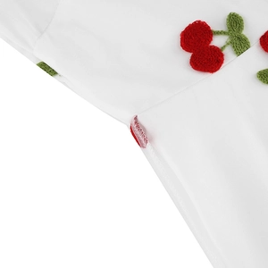Gros plan de la broderie cerise rouge sur robe blanche avec détails de couture précis