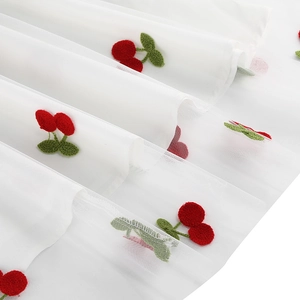 Gros plan sur un tissu en maille blanche avec broderies de cerises rouges et feuilles vertes