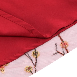 Detail of red V-neck dress featuring delicate floral embroidery on white sheer mesh hemline