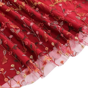Macro detail of delicate floral and butterfly embroidery on dark red tulle dress fabric