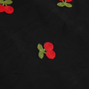 Détail du tissu en maille noire avec broderie de cerises rouges 3D et feuilles vertes