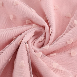 Détail du tissu en maille rose avec motif de cœurs floqués et texture de drapé doux