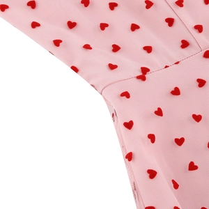 Détail du tissu en tulle rose avec motifs de cœurs rouges et coutures précises sur la robe