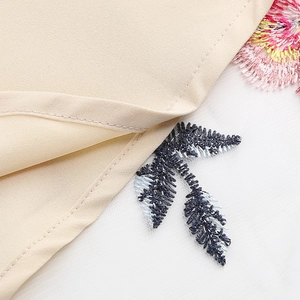 Macro de broderies florales roses et feuilles bleues sur une robe vintage en résille