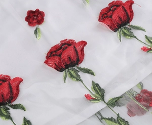 Detailed close-up of red rose floral embroidery on white mesh fabric for cocktail dress