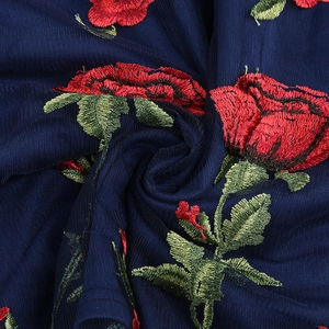 Vue détaillée de broderies roses rouges sur tissu en maille bleu marine ajouré