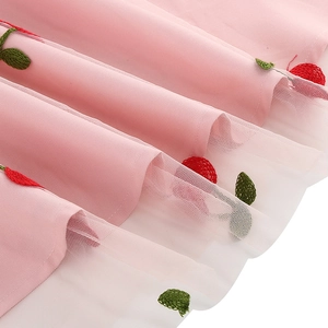 Gros plan de la broderie cerise sur satin rose et tulle blanc de la robe en maille