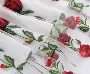 Detail of white mesh fabric with red rose and green leaf embroidery on the dress