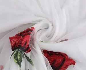Detailed close-up of delicate red rose embroidery on white mesh fabric for cocktail dress