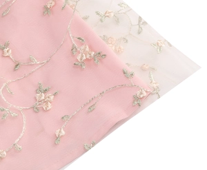 Close-up of exquisite floral rose embroidery on delicate tulle lace fabric in pink and ivory