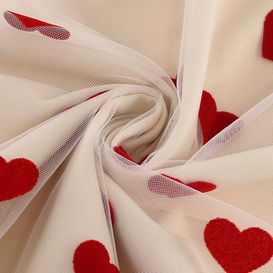 Vue détaillée du tissu en tulle beige avec des motifs de cœurs rouges floqués en relief