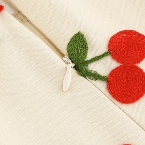 Détail macro de broderie cerise rouge et fermeture éclair sur robe beige en coton