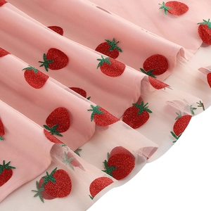Gros plan sur le tissu en tulle rose avec paillettes fraises rouges et broderies vertes