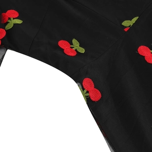 Détail de la broderie cerise et du tissu en maille sur une robe noire vintage