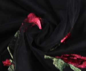 Close-up of black mesh fabric with red rose embroidery and green leaf details