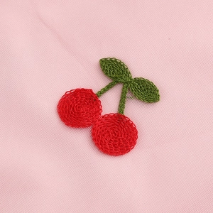 Gros plan d'une broderie de cerises rouges sur tissu en maille rose avec détails