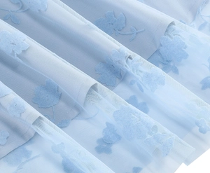 Gros plan sur le tissu en tulle bleu clair avec motif floral floqué et texture maille