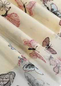 Gros plan d'une broderie papillon complexe sur un tissu de tulle mesh blanc cassé