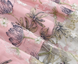 Close-up detail of delicate floral embroidery on pink mesh fabric for elegant dresses