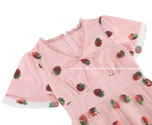 Close-up of pink V-neck dress with sequin strawberry patterns and delicate lace trim