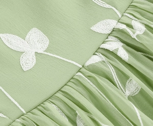 Detailansicht der weißen floralen Stickerei auf hellgrünem plissiertem Chiffon-Stoff
