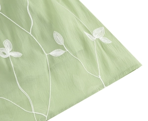 Detaillierte Nahaufnahme von hellgrünem Chiffonstoff mit zarten weißen Blumenstickereien