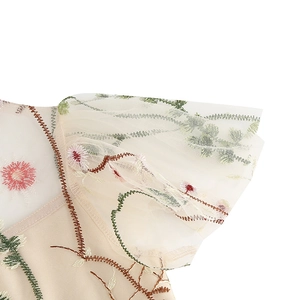Detail of red floral embroidery on beige mesh fabric with decorative brown wavy stitching