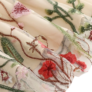 Detailed macro view of colorful floral embroidery on light beige mesh fabric