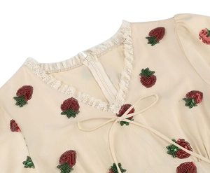 Close-up of V-neck with lace trim, bow tie and red sequin strawberry embroidery on dress