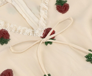 Macro detail of V-neckline with lace trim and sequined strawberry embroidery motifs