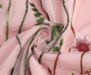 Detail shot of pink mesh fabric with intricate green floral embroidery and fine textures