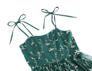 Detailed close-up of dark green tulle dress with white floral embroidery and bow straps