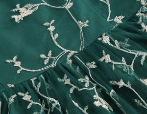 Detailed close-up of dark green mesh dress with white floral embroidery and waist pleats