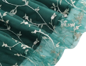 Detail view of dark green tulle mesh dress with silver vine embroidery and pleated layers