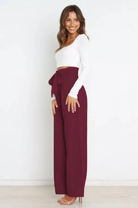 Detailed view of high waisted wide leg trousers in burgundy with a large stylish waist bow