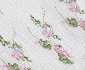 Close-up of white wrinkled mesh fabric with pink and green floral embroidery detail