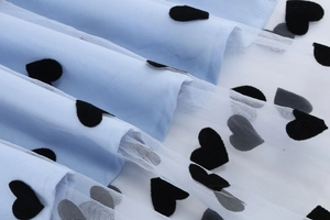 Detail of light blue mesh fabric with black velvet heart embroidery and tulle layering