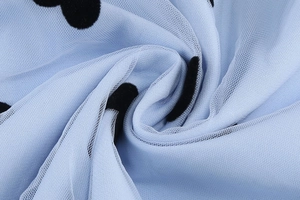 Detail of light blue mesh fabric featuring black flocked polka dots and sheer texture