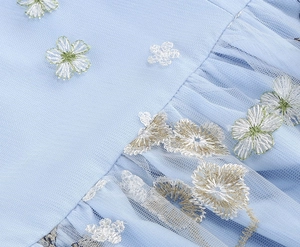 Detailed macro view of light blue mesh fabric with delicate floral embroidery on dress