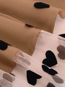 Detail des Vintage Kleidsaums mit braunem Stoff und weißem Netz mit schwarzen Herzen