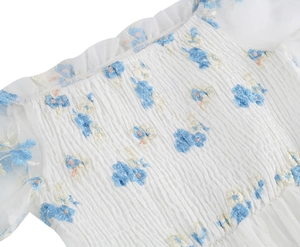 Close-up of floral embroidery on a white mesh dress with smocked bodice details