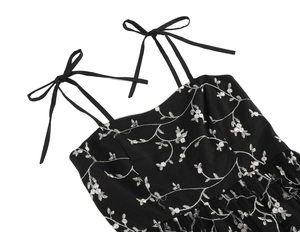 Detail of floral embroidery and bow-tie shoulder straps on a black mesh dress