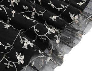 Close-up of elegant floral embroidery with silver and pink threads on black mesh fabric